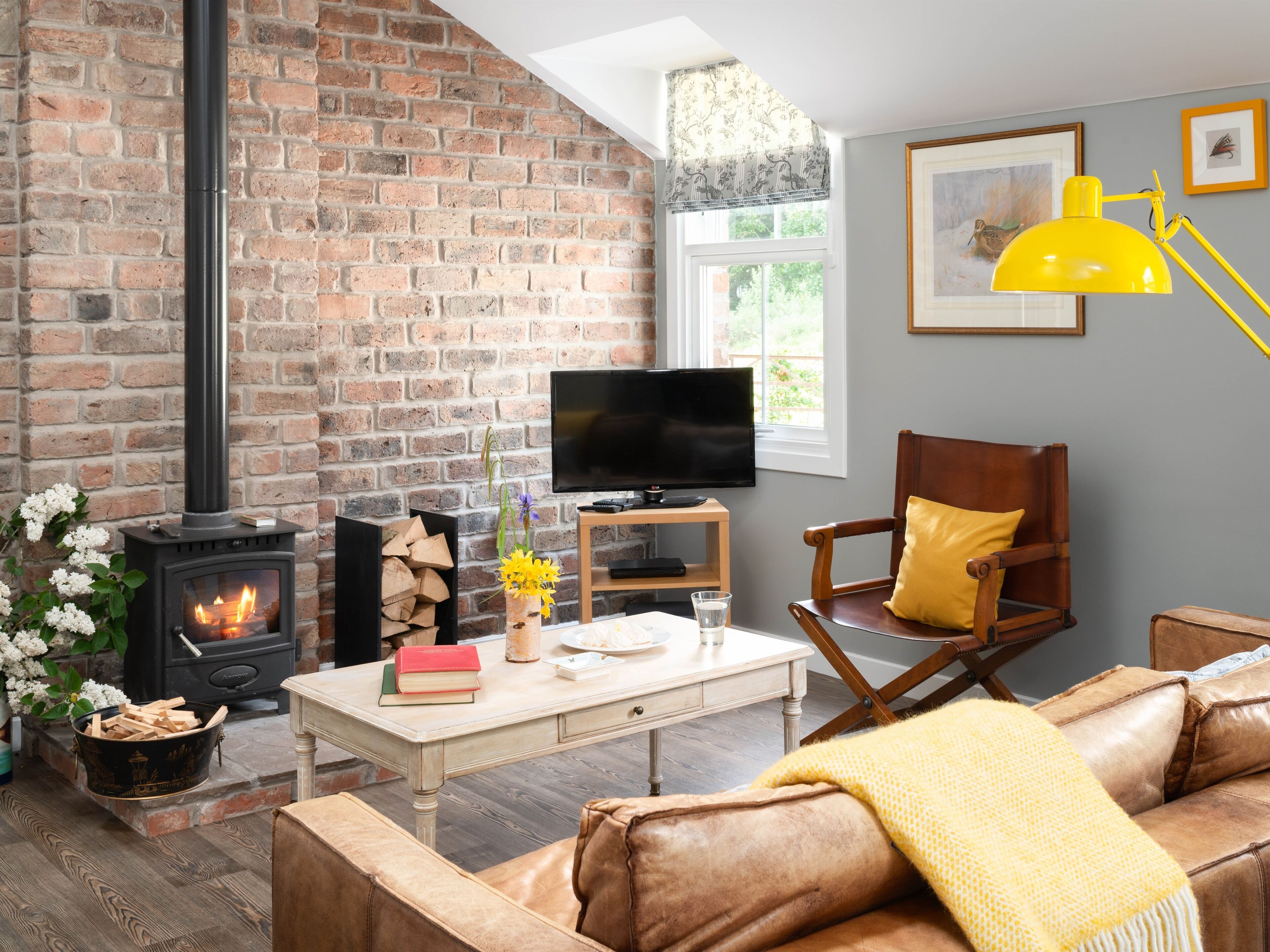 Ein gemütliches Wohnzimmer mit Kamin aus Backstein, einem Fernseher, einem Holzstuhl und einem Ledersofa.