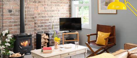 Ein gemütliches Wohnzimmer mit Kamin aus Backstein, einem Fernseher, einem Holzstuhl und einem Ledersofa.