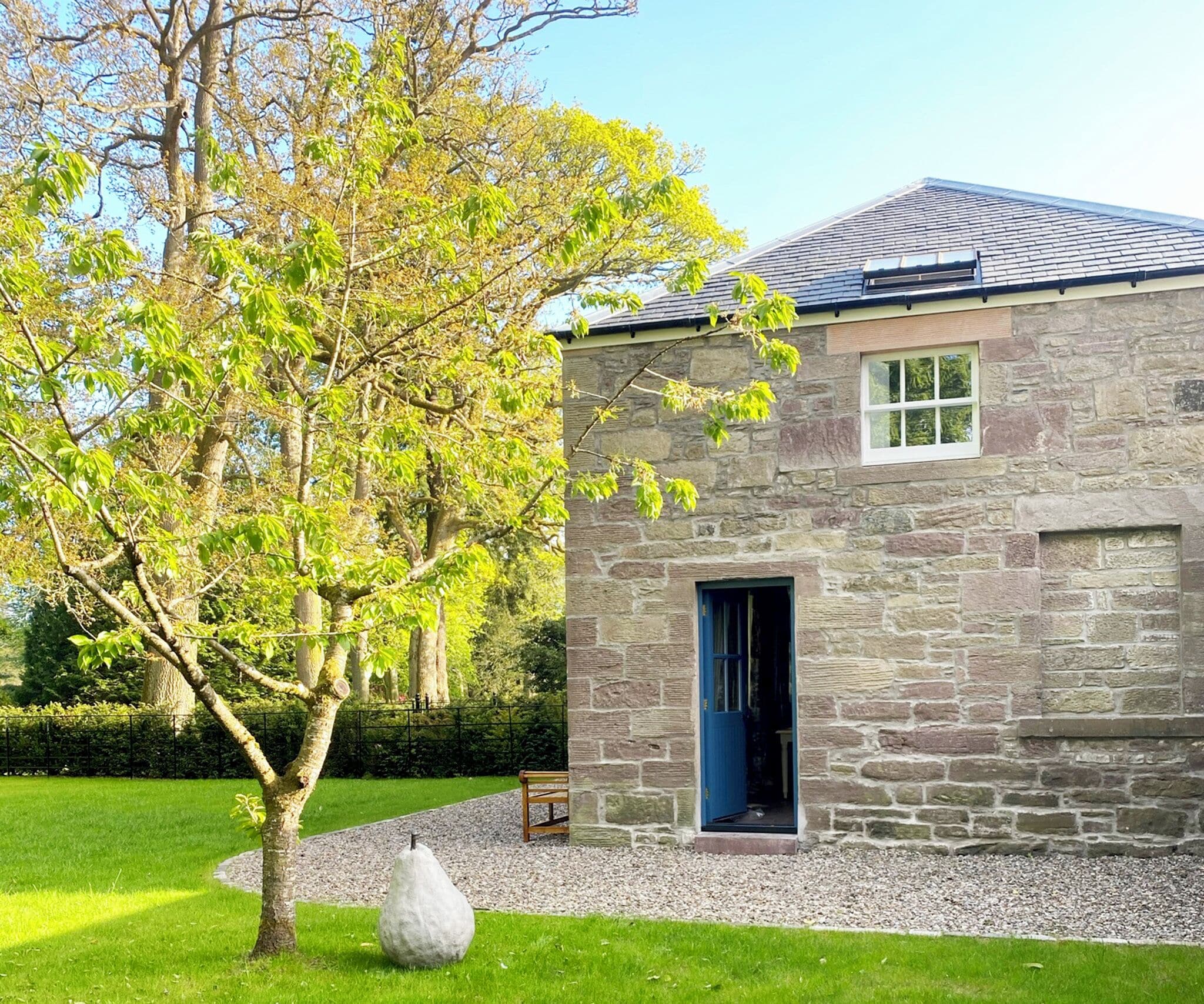 A stone building with a blue door, surrounded by a well-maintained lawn and a tree.