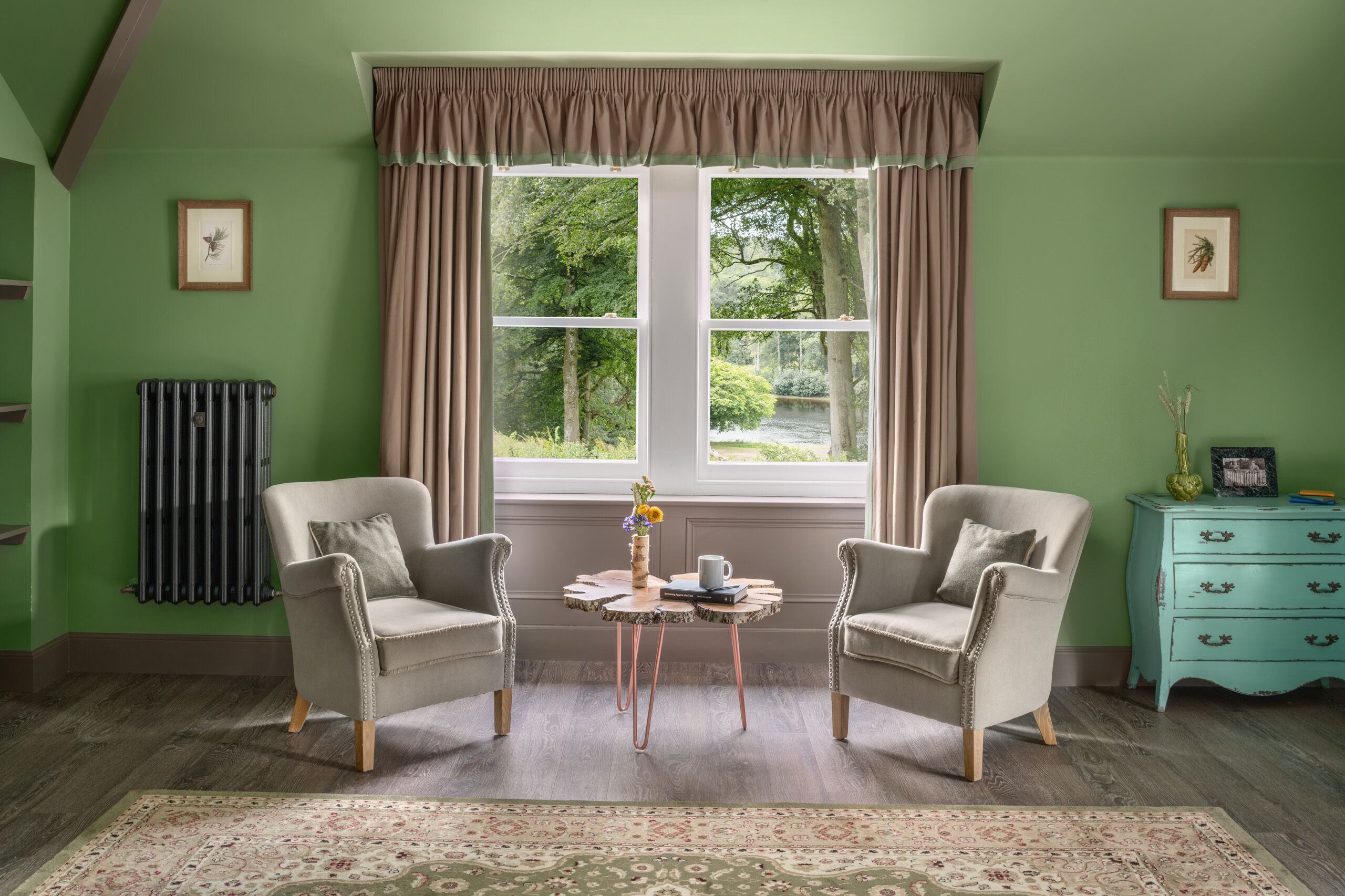 A room with two armchairs, a small table, a radiator, and a window with curtains.