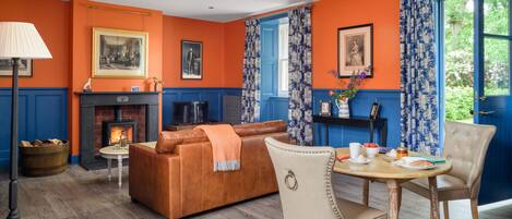 Ein Wohnzimmer mit Kamin, orangefarbenen Wänden, blauen Akzenten, einem braunen Ledersofa, einem Holztisch und einem Essbereich mit Stuhl und Tisch.