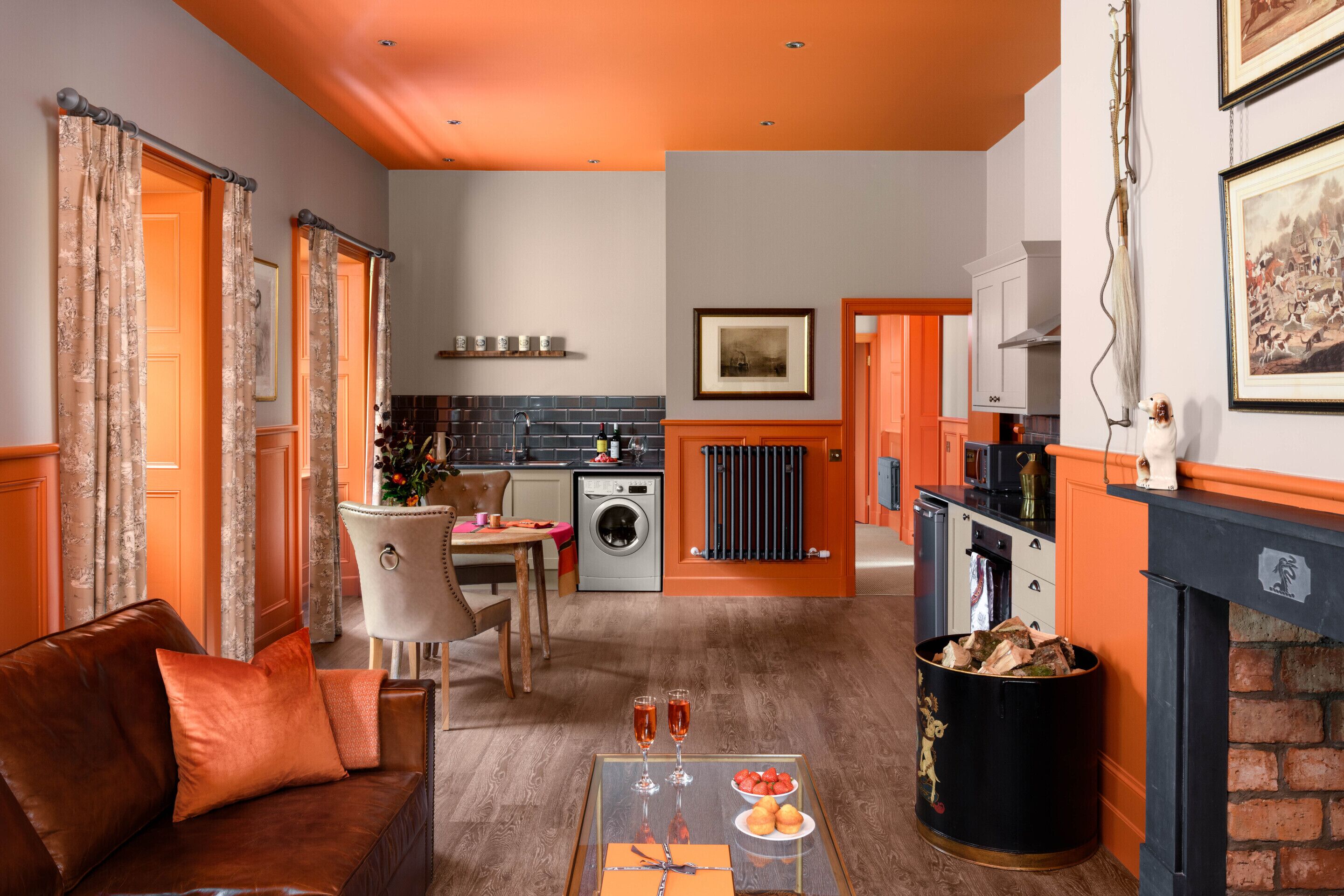 A living room with a brown leather sofa, a dining table with chairs, a kitchen area with a washing machine, and a fireplace.