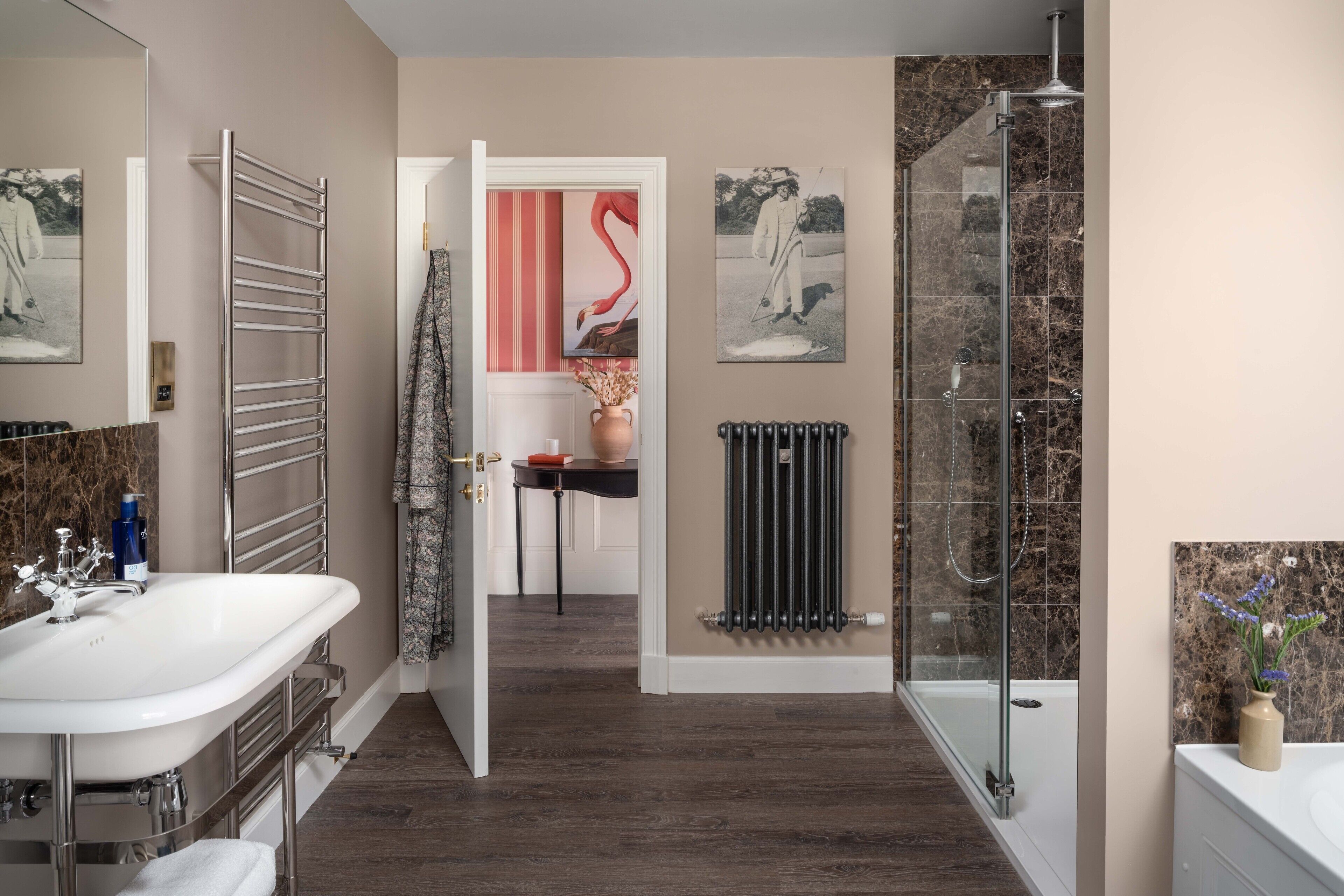 A modern bathroom with a large mirror, a double sink, a glass shower enclosure, and a radiator.