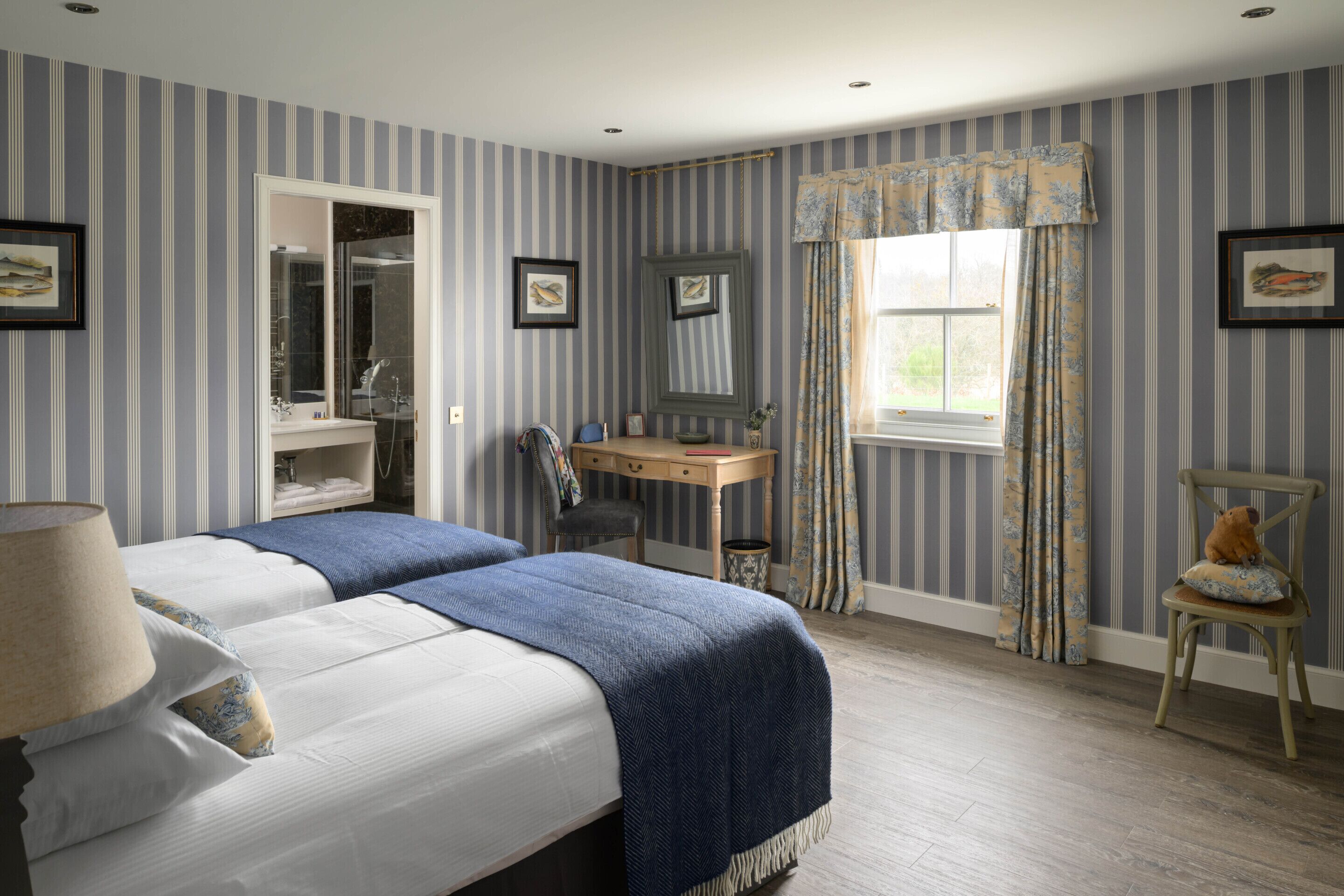 A hotel room with two beds, a desk, a chair, a window with curtains, and a mirror.