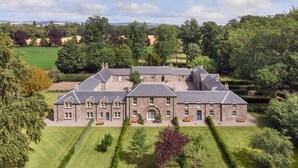 Een groot, stenen gebouw met verschillende vleugels, omgeven door verzorgde gazons en bomen.