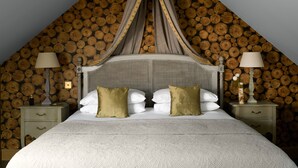 Een slaapkamer met een hemelbed, een wand van houten balken, twee nachtkastjes met lampen en een groot sprei.