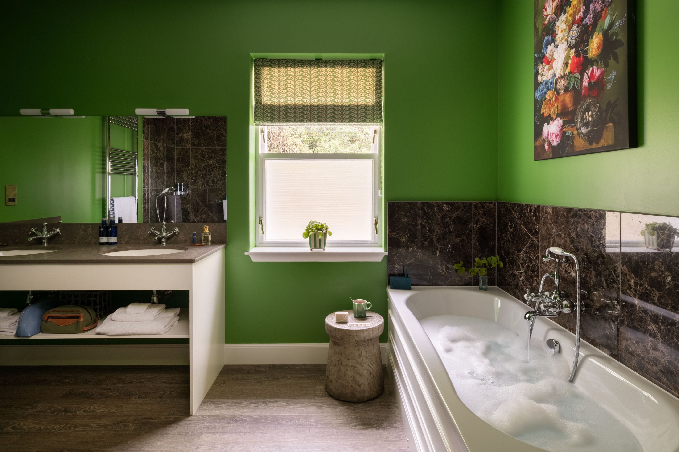 A bathroom with green walls, a large bathtub, a window with a view, and a mirror above the sink.