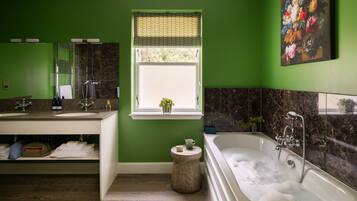 Un baño con paredes verdes, una bañera grande, un ventanal con vistas y un espejo sobre el lavabo.