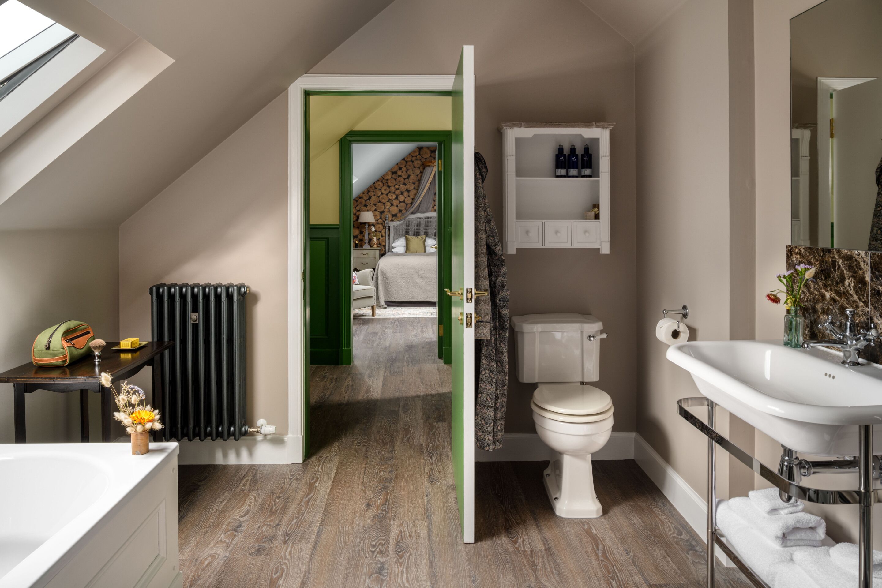 Ein modernes Badezimmer mit Waschbecken, Toilette und Dusche. Ein Heizkörper, ein kleiner Tisch mit Toilettenartikeln und eine grüne Tür, die zum Schlafzimmer führt, sind ebenfalls vorhanden.