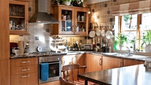 A kitchen with wooden cabinets, a built-in oven, a stove, and a large island with a sink. - Little Red Rooster Rest and Spa (Tenby)