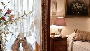 A bedroom with a bed, a nightstand with a lamp, a dresser, and a window with sheer curtains. - Little Red Rooster Rest and Spa (Tenby)