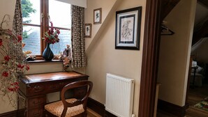 A wooden desk with a chair, a radiator, and framed artwork on the wall. - Little Red Rooster Rest and Spa (Tenby)
