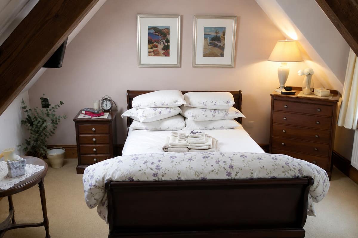 Une chambre à coucher avec un lit en bois, une table de chevet avec une lampe, une commode et deux tableaux encadrés au mur.