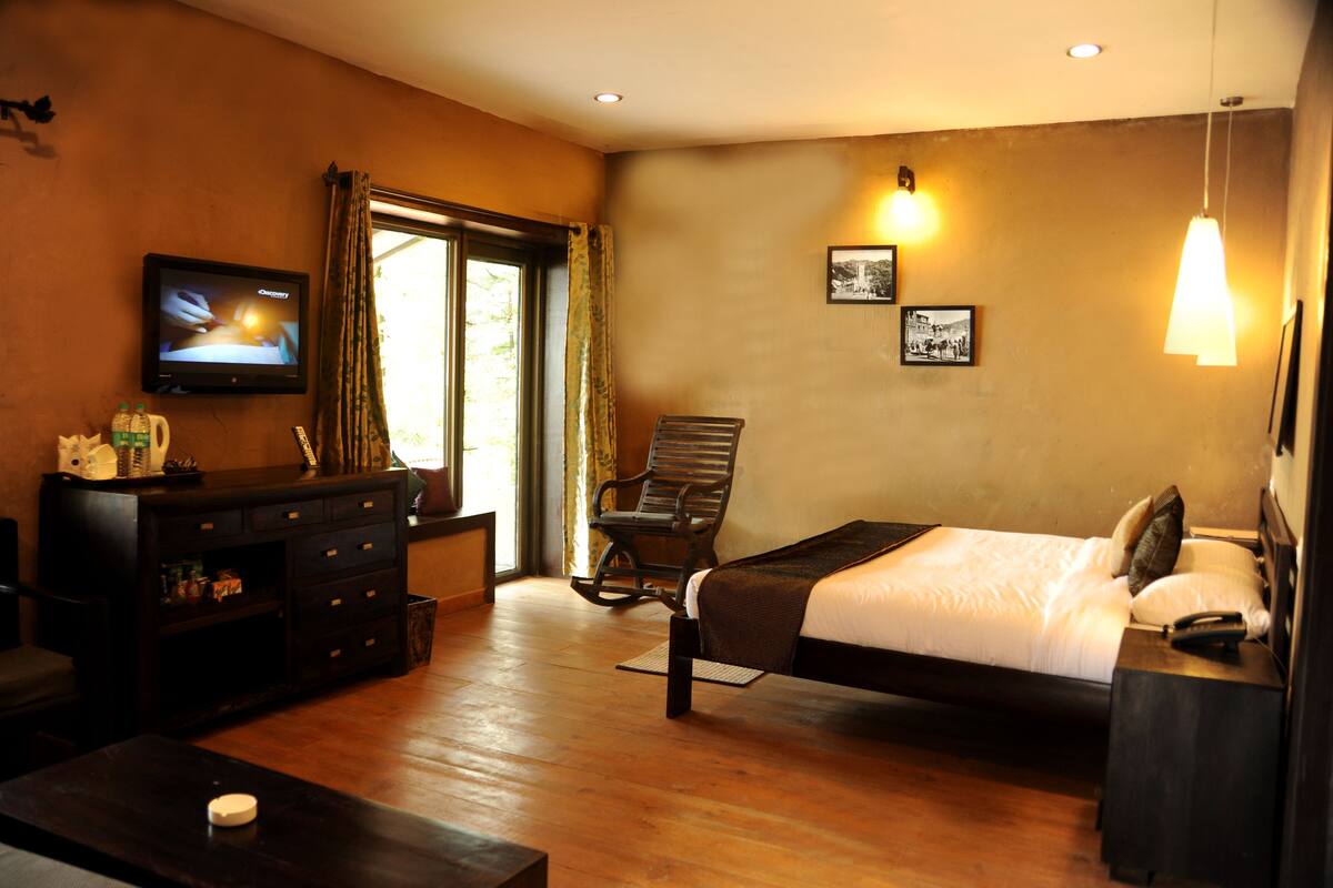 A hotel room with a bed, a TV, a desk, a chair, and a window with curtains.
