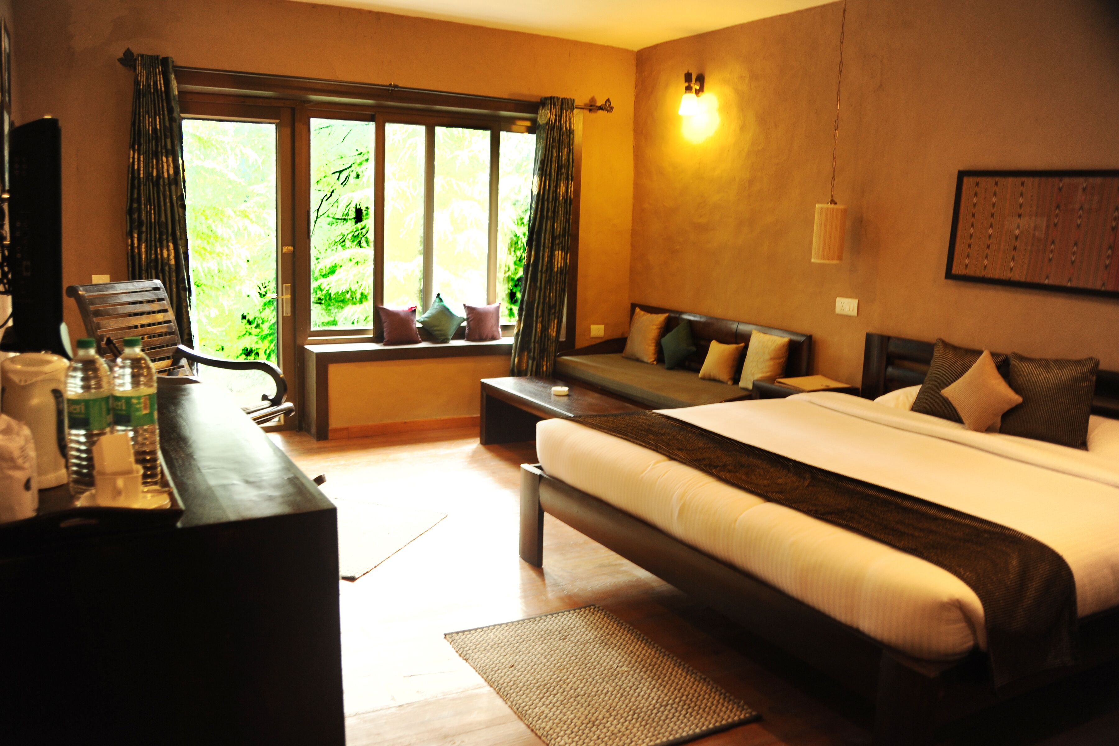 A hotel room with a large bed, a desk with a chair, a window with curtains, and a wall-mounted light fixture.