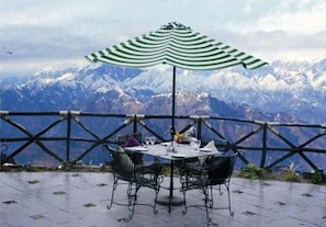 Una mesa con cuatro sillas y un paraguas verde y blanco a rayas, con montañas nevadas de fondo.