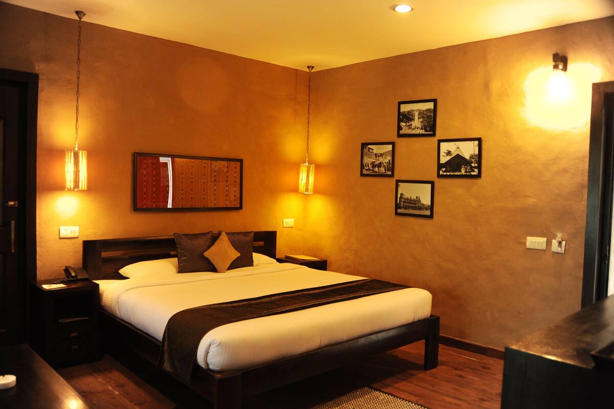 A hotel room with a large bed, bedside tables, a nightstand, wall-mounted light fixtures, and framed pictures on the wall.