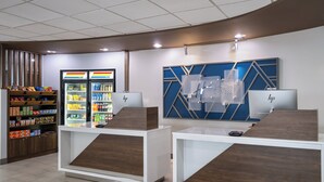 A modern reception area with a counter, a refrigerator stocked with beverages, and a display wall with a geometric design. - Holiday Inn Express Toledo North by IHG (Toledo)