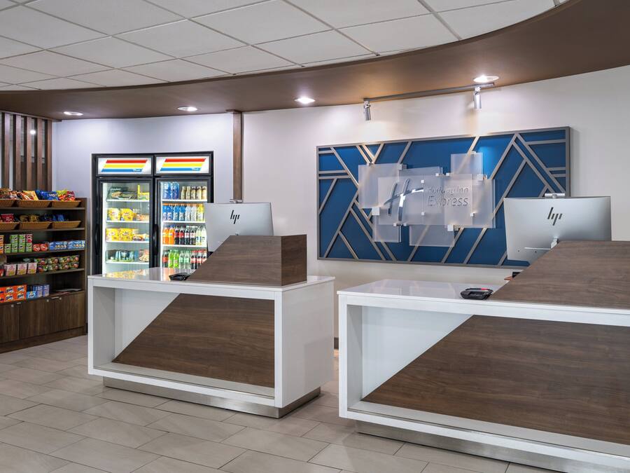 Una moderna zona de recepción con mostrador, un refrigerador lleno de bebidas y una pared decorativa con diseño geométrico.