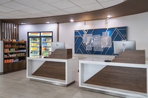 Un espace d’accueil moderne comprenant un comptoir, un réfrigérateur rempli de boissons et un mur décoratif orné d’un motif géométrique.