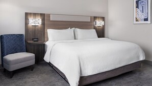 A modern hotel room with a large bed, a small seating area, and wall-mounted lighting. - Holiday Inn Express Toledo North by IHG (Toledo)