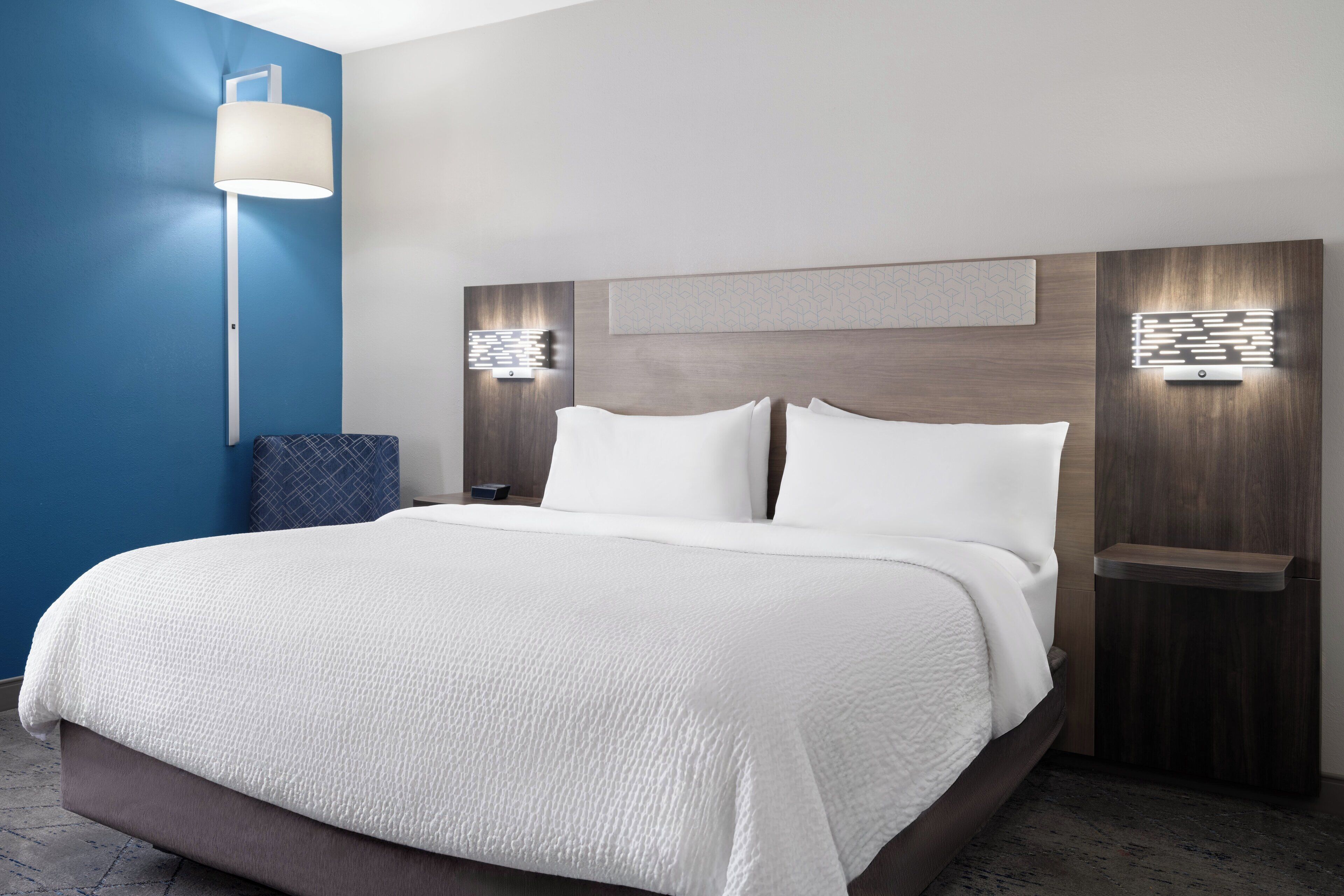 Une chambre d’hôtel moderne avec un grand lit, une table de chevet avec une lampe et un luminaire fixé au mur.