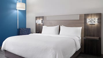 Une chambre d’hôtel moderne avec un grand lit, une table de chevet avec une lampe et un luminaire fixé au mur.
