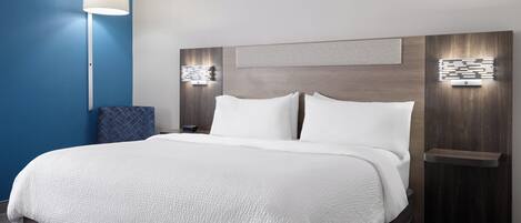 Une chambre d’hôtel moderne avec un grand lit, une table de chevet avec une lampe et un luminaire fixé au mur.