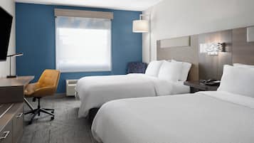 Een hotelkamer met twee bedden, een bureau, een stoel, een raam met zonwering en een telefoon aan de muur.