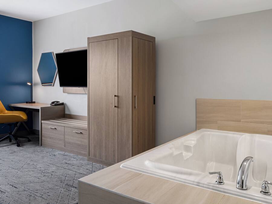 Een moderne hotelkamer met een houten garderobe, een bureau met stoel, een ruim bad en een wandgemonteerde flatscreen televisie.