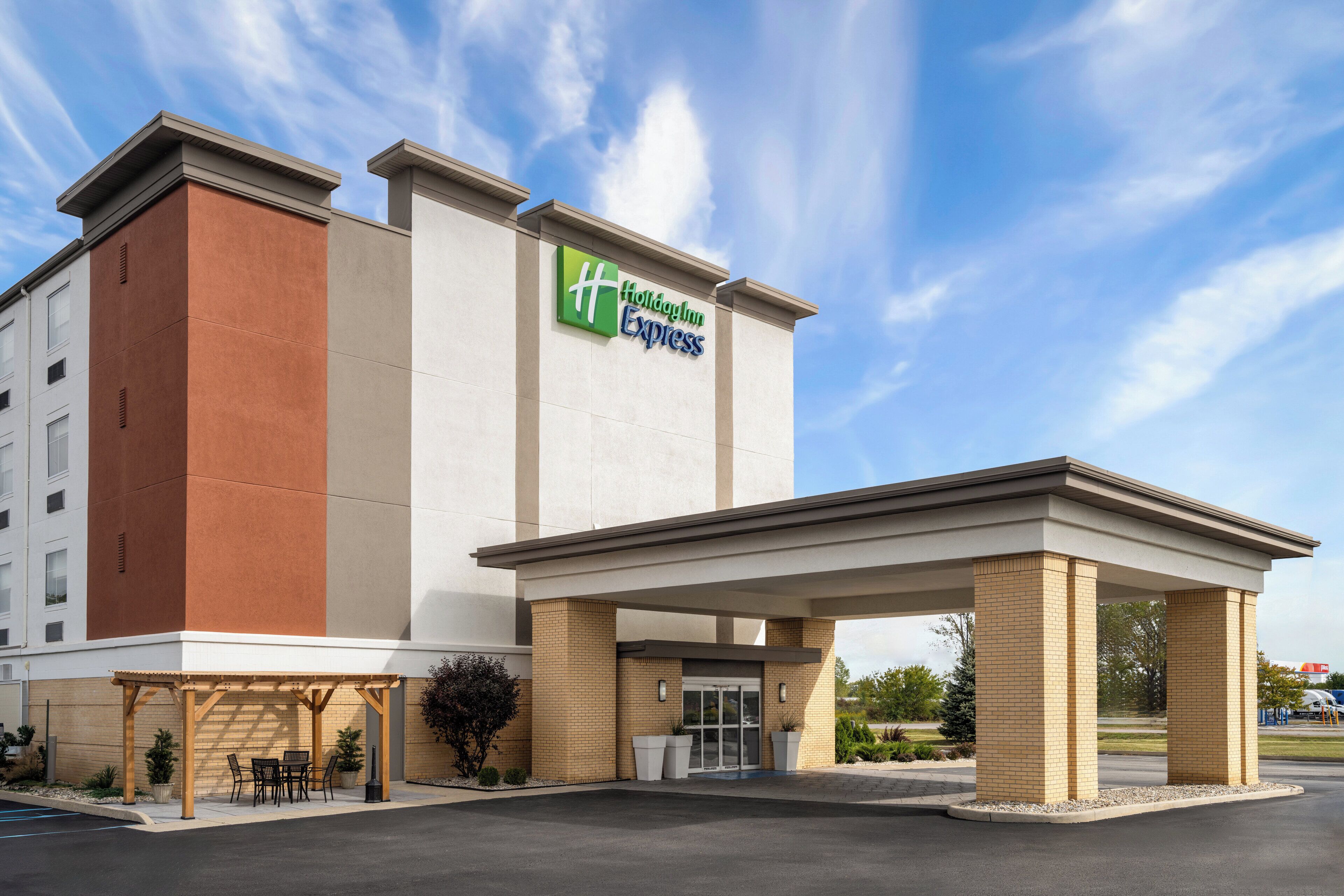 Edificio de Holiday Inn Express con un acceso cubierto, asientos exteriores y un cielo despejado.
