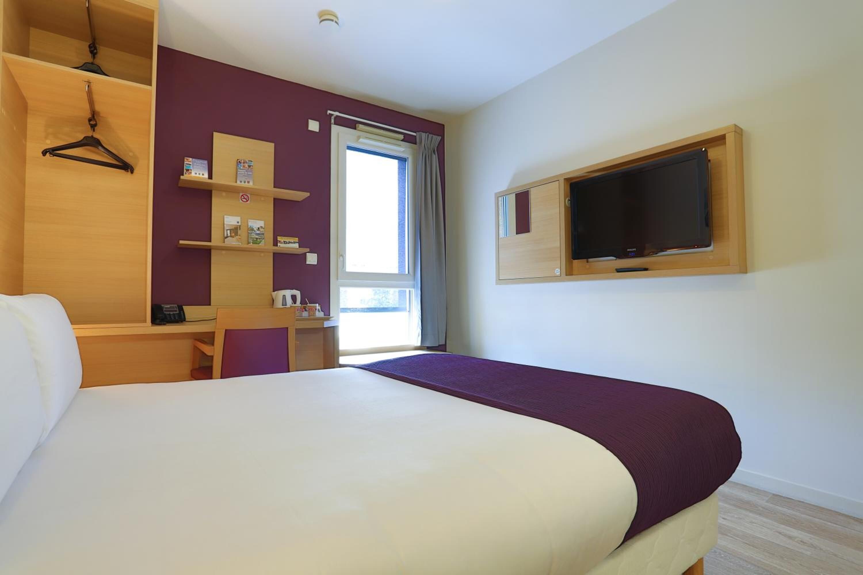 A hotel room with a bed, a desk, a TV, and a window with curtains.