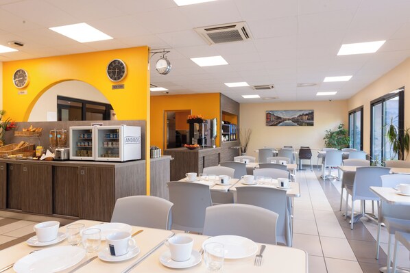 A modern dining area with tables set for breakfast, a counter with a coffee machine, and a clock on the wall. - Eastlodge Lyon Est Eurexpo (Saint-Priest)