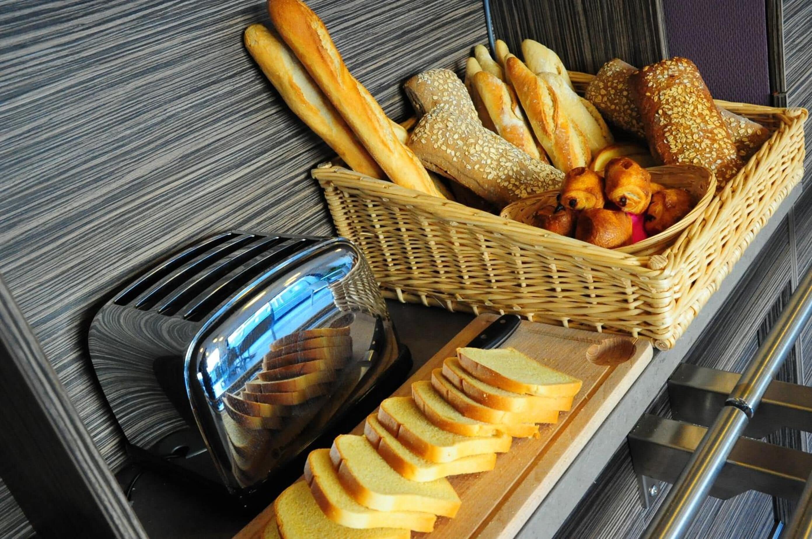Een ontbijtbuffet met diverse broden, een broodrooster en plakken brood op een houten plank.