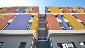 Ein mehrgeschossiges Gebäude mit moderner Architektur, das eine symmetrische Fassade mit abwechselnd farbigen Paneelen aufweist.