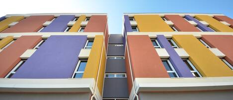 Un edificio de varios pisos con un diseño arquitectónico moderno, que presenta una fachada simétrica con paneles de colores alternados.