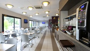 Eine geräumige Cafeteria mit mehreren Tischen und Stühlen, einer Theke mit einer Kaffeemaschine und einem an der Wand befestigten Fernseher.