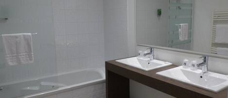 A modern bathroom with two sinks, a bathtub, and a large mirror.