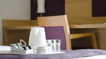 Une chambre d’hôtel bien rangée, avec un lit, une table de chevet sur laquelle se trouvent une machine à café, des verres et une boîte de mouchoirs.