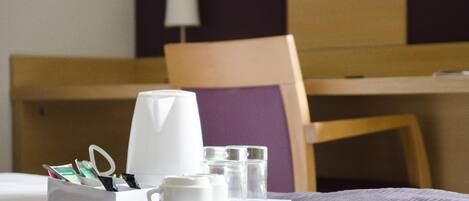 A neatly arranged hotel room with a bed, a bedside table with a coffee maker, glasses, and a tissue box.