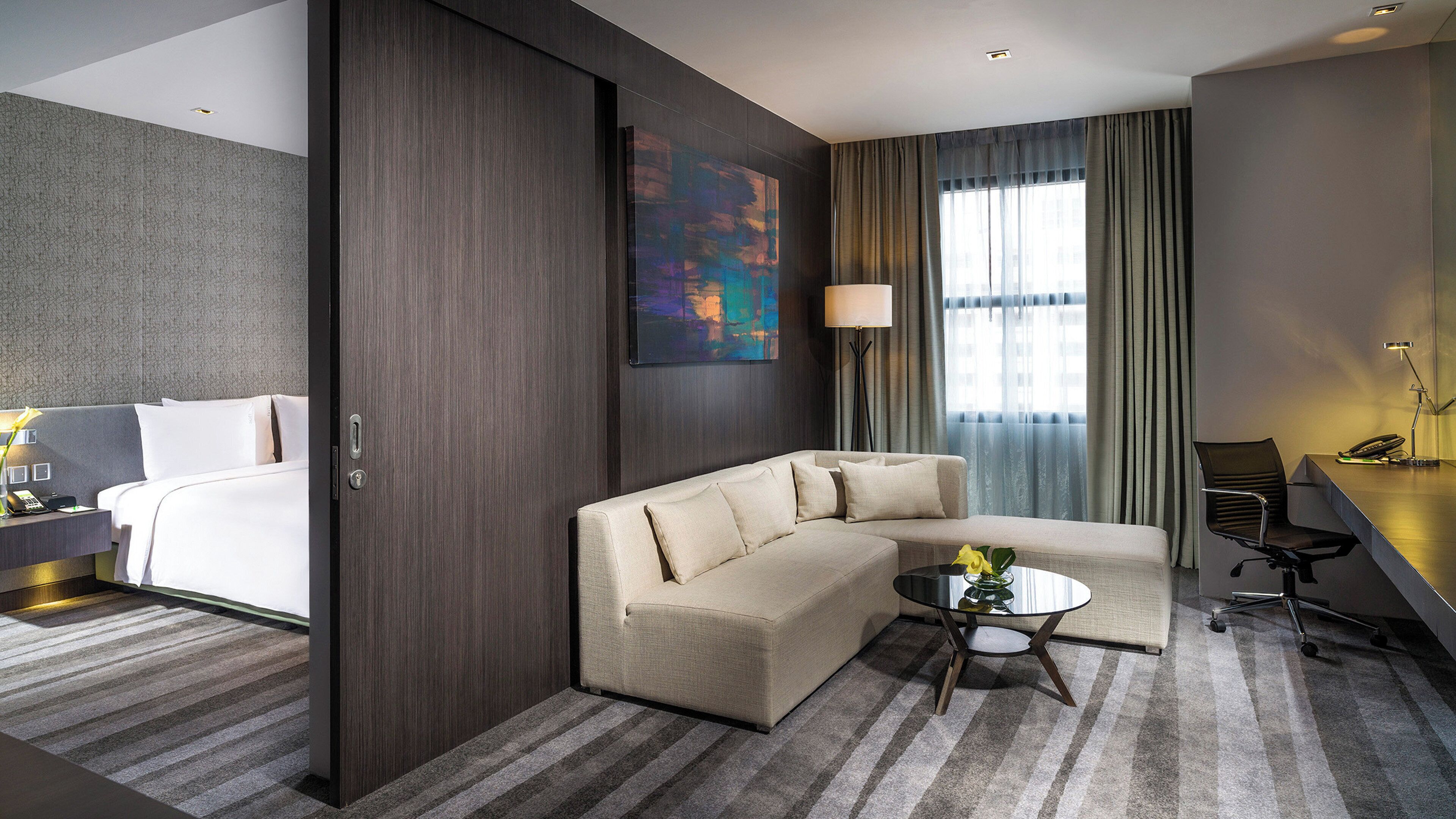 Una habitación de hotel con cama, sofá, escritorio, lámpara y un cuadro.