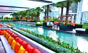 A rooftop pool area with seating and greenery, surrounded by modern buildings.