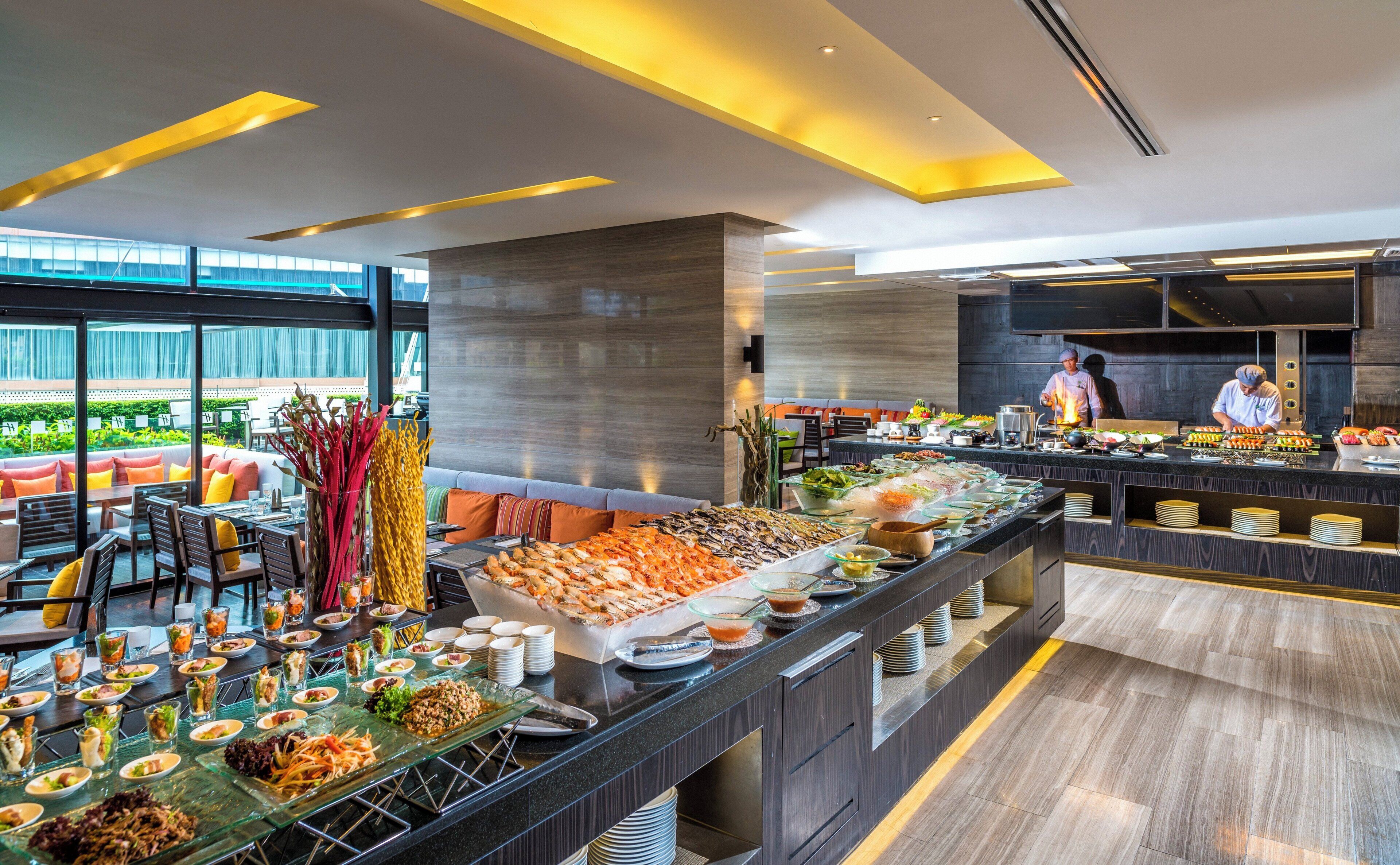A buffet setup with a variety of food items, a seating area with tables and chairs, and a kitchen area with chefs preparing food.