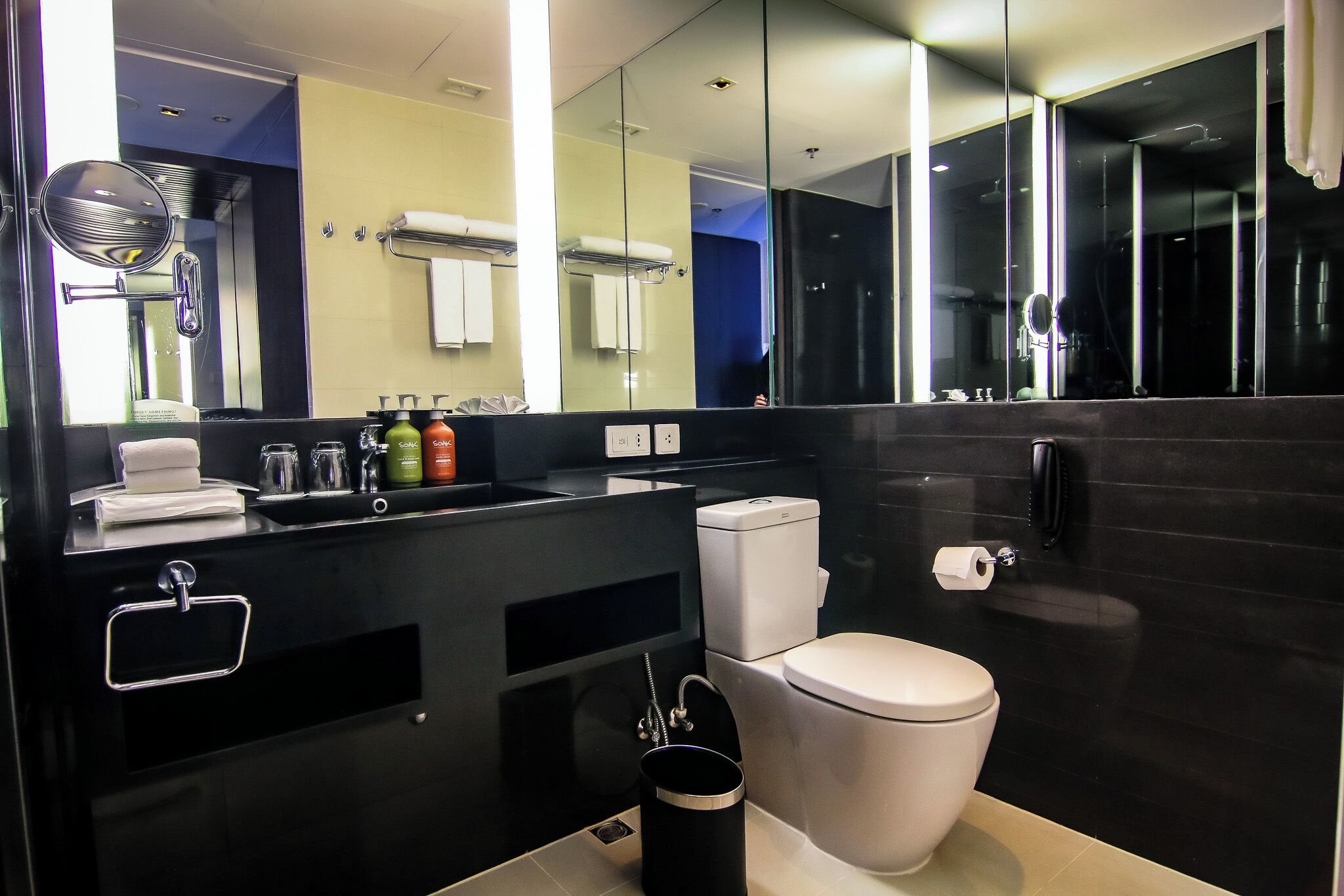 Une salle de bain moderne avec un plan de toilette noir, des toilettes, un lavabo et un grand miroir.