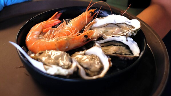 A black bowl containing a cooked shrimp and several oysters.