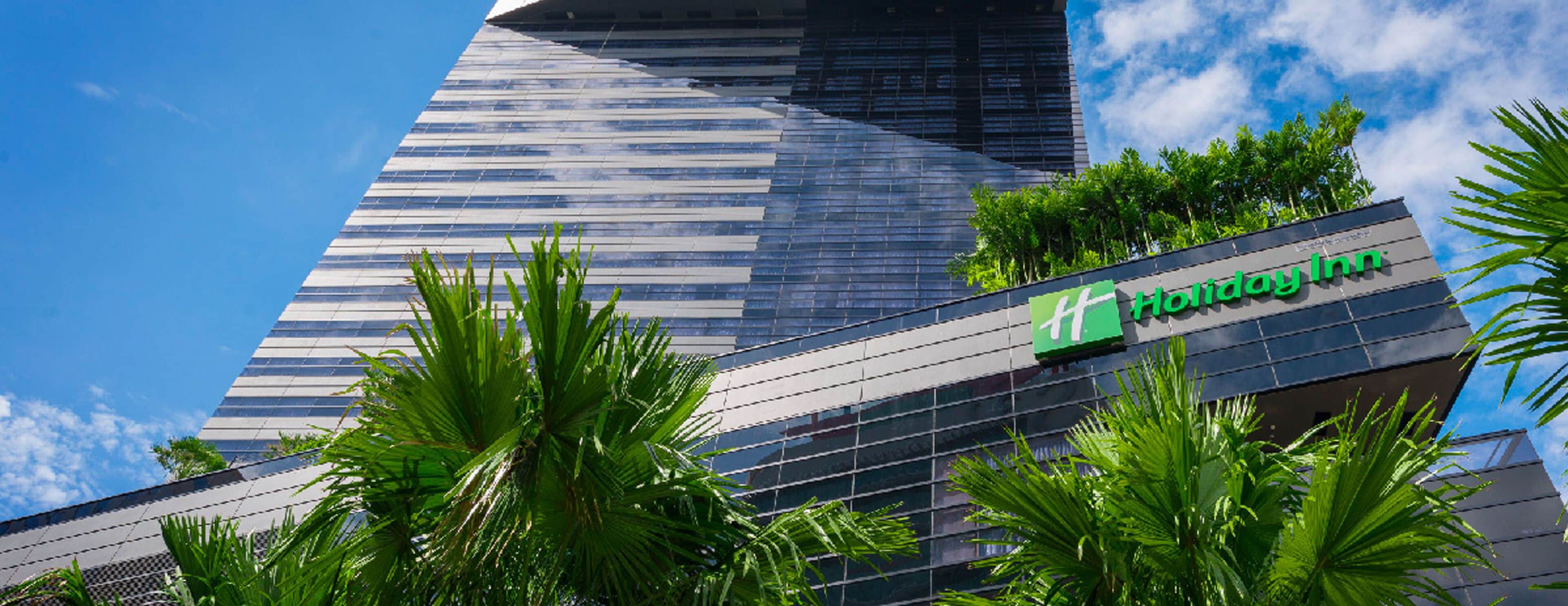 A Holiday Inn hotel with a modern glass facade and palm trees in the foreground.