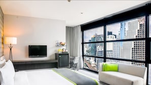 A hotel room with a bed, a sofa, a TV, a desk with a lamp, and a large window with a city view. - Holiday Inn Bangkok Sukhumvit by IHG (Bangkok)