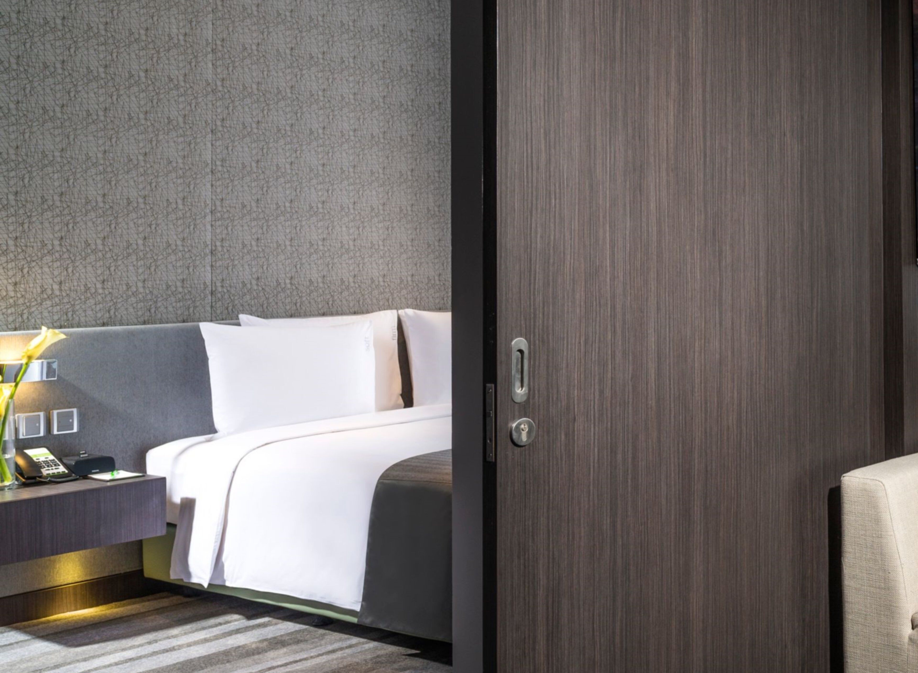 Ein Hotelzimmer mit Bett, Nachttisch, Lampe und einer Tür.