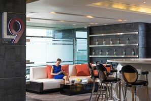 Ein moderner Loungebereich mit einer Couch, Barhocker und einer Bar mit Flaschenregalen.