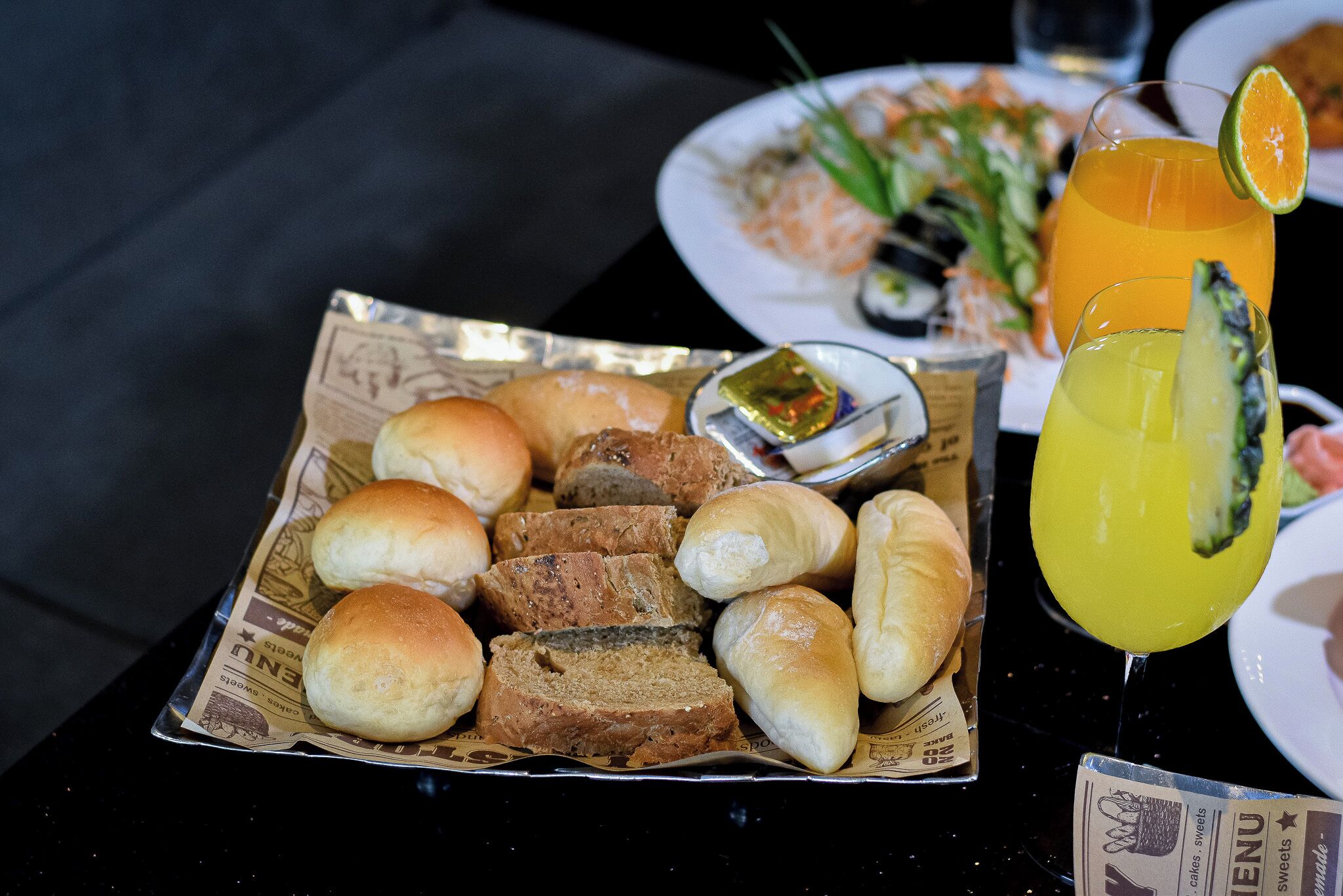 A tray of assorted bread rolls and a glass of orange juice on a table.